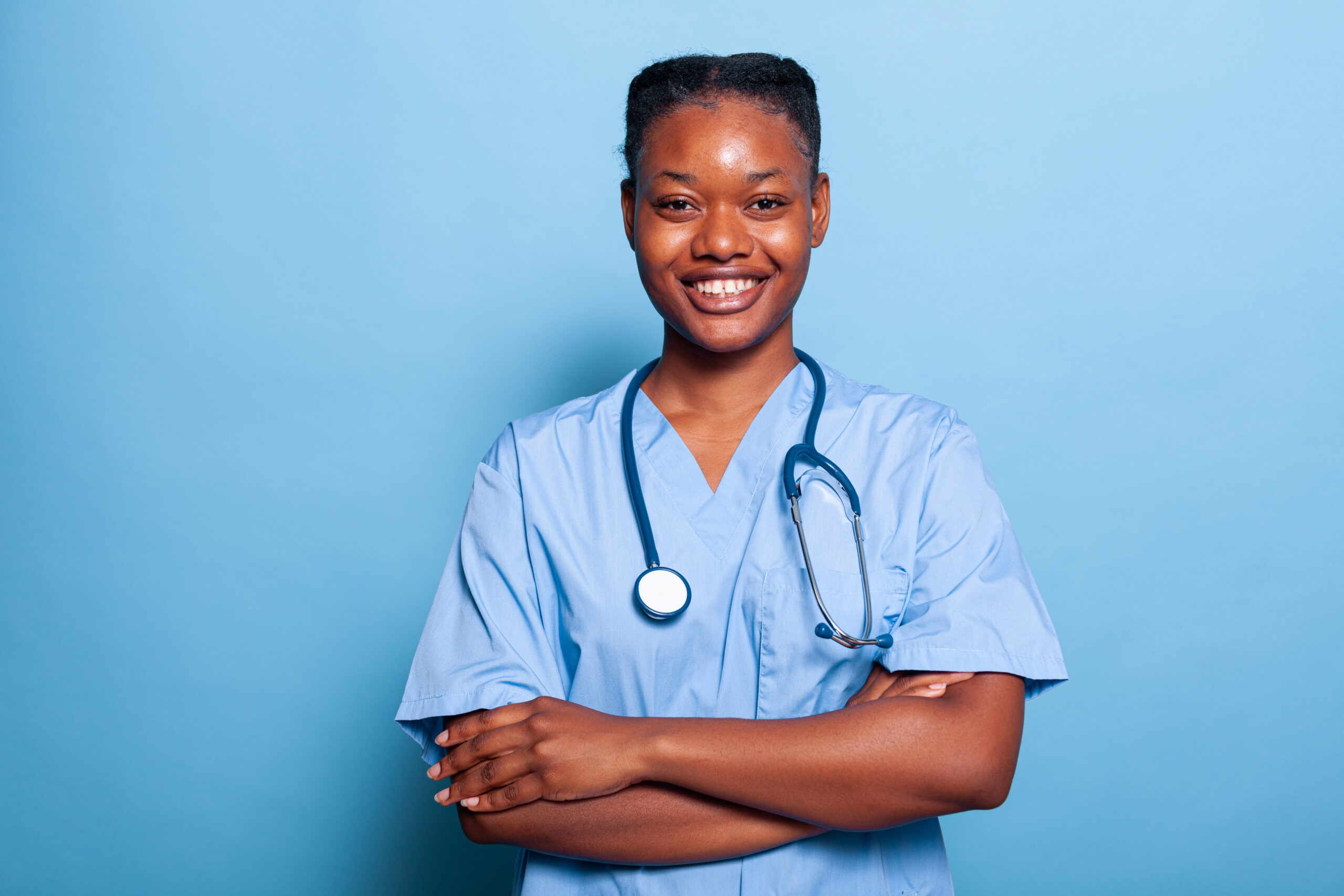 Portrait of african american practitioner nurse smiling at camera working at illness expertise in studio with blue background. Therapist woman in medical uniform and stethoscope. Medicine concept